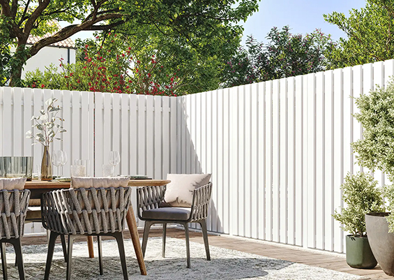 Clôture aluminium blanc à lames verticales pleines, design lumineux et moderne autour d'une terrasse jardin avec table et chaises, ambiance contemporaine claire en extérieur bordelais.