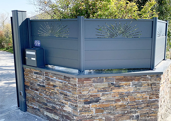 Clôture aluminium gris anthracite ajourée avec motifs soleil décoratifs, sur muret pierre multicouche, portillon avec boîte aux lettres intégrée, style personnalisé moderne en Gironde.