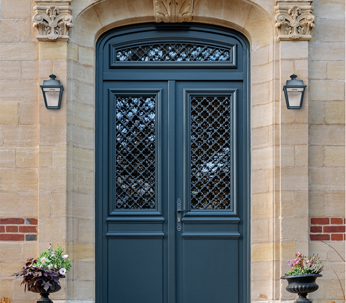 Porte d’entrée en bois bleu foncé à deux vantaux avec vitrages décoratifs sur une façade en pierre